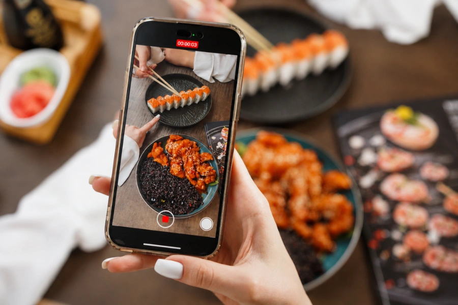 Person recording sushi and a chicken rice dish on a smartphone at a restaurant.